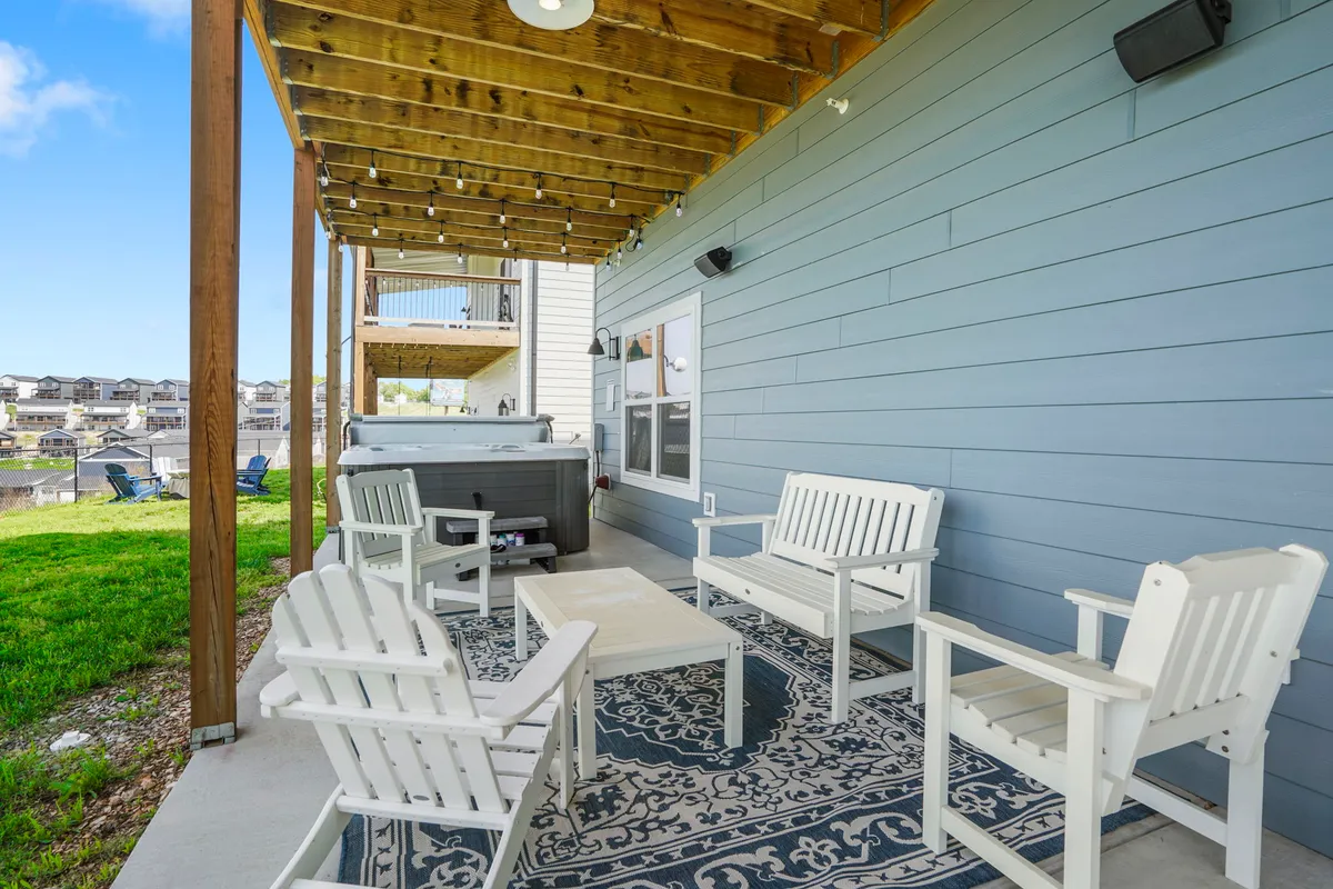 An inviting exterior space featuring an outdoor seating area with a decorative rug and a private hot tub set on a cozy patio. Lush surroundings hint at scenic lake views, and the setup feels perfect for relaxing mornings with coffee or stargazing at night.