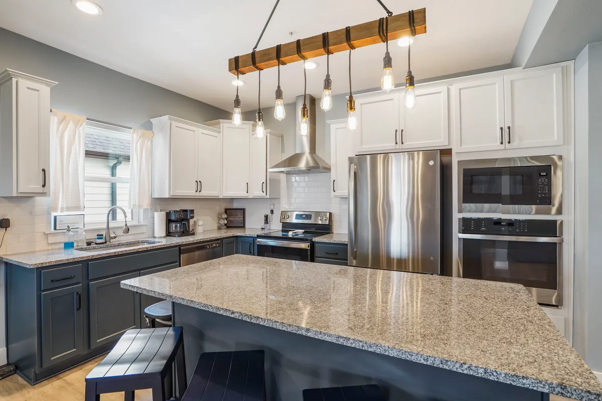 A close-up of the fully equipped kitchen showcases granite countertops, blue cabinetry, stylish hanging light fixtures, and stainless steel appliances. The setup is perfect for preparing group meals, with ample space for cooking and socializing.