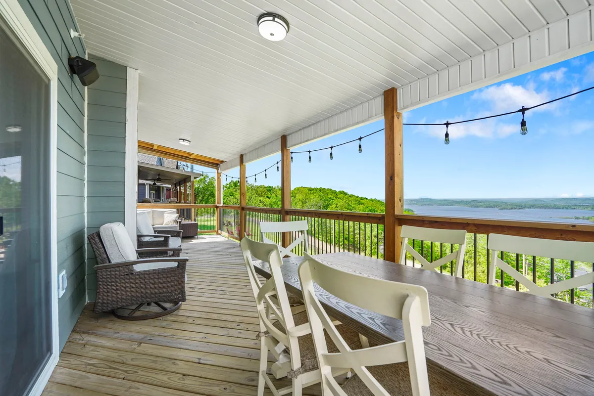 An inviting outdoor dining area on a deck, illuminated by hanging lights with views of the landscape. The space is set up for al fresco meals, relaxing morning coffee, and family gatherings, emphasizing the connection to nature and comfort.