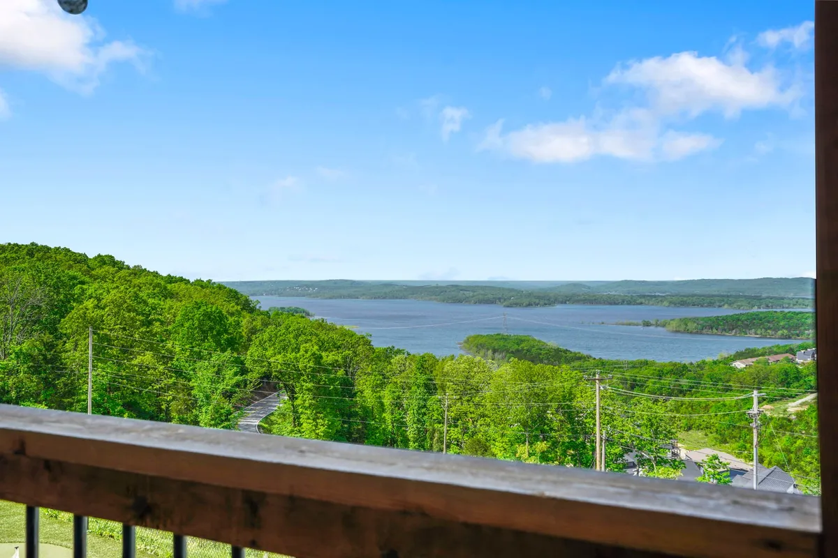 A panoramic view of Table Rock Lake framed by lush green trees, distant hills, and a clear blue sky. The landscape exudes tranquility and invites activities such as swimming, kayaking, and enjoying nature.