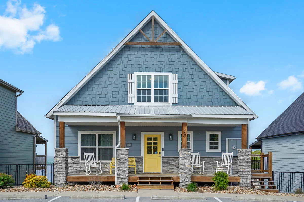 A welcoming front porch with a cheerful yellow door, rock accents, and classic rocking chairs. The scene exudes hospitality and offers space for gathering, watching sunsets, or enjoying quiet mornings together.