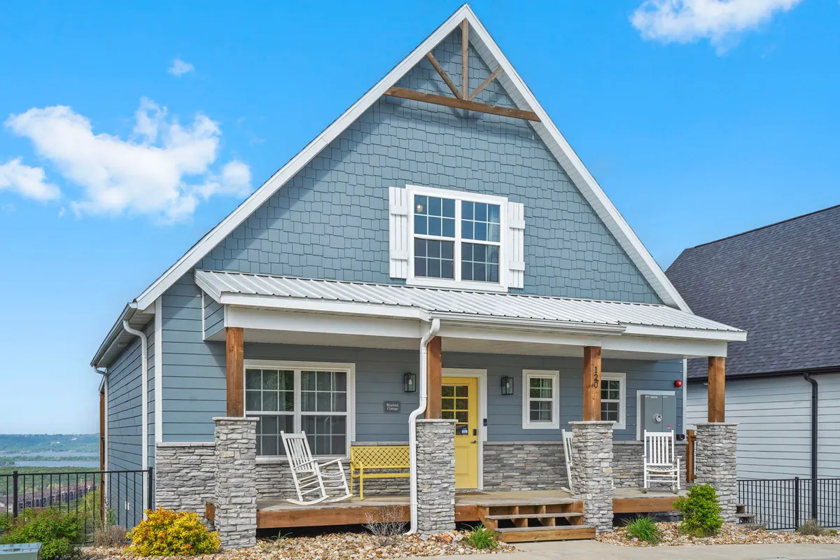 A cheerful and welcoming front porch with stone pillars, a bright yellow door, and rocking chairs. The space is ideal for enjoying morning coffee, greeting neighbors, or simply taking in the tranquil surroundings.